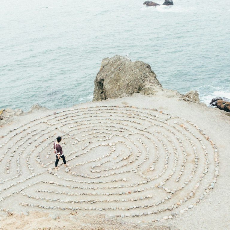 Eine Person in einem Steinlabyrinth am Meer steht nahe einer Felsenküste.