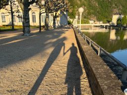 Zwei Schatten halten sich an den Händen, auf einem Weg am Wasser in Bad Ems bei Sonnenuntergang.