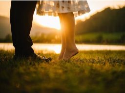 Zwei Personen stehen sich nahe, während die Sonne im Hintergrund untergeht.