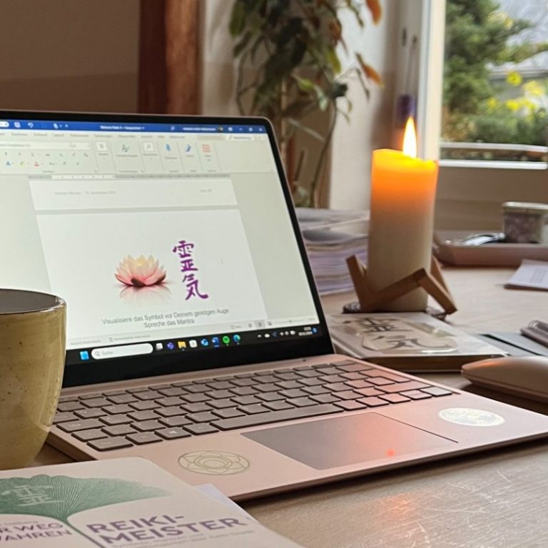 Tisch mit Laptop, Kaffeetasse, Kerze und Unterlagen in einem hellen Raum.