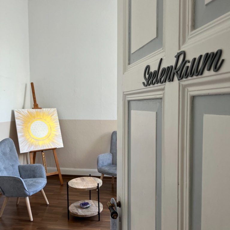 Praxis Bad Ems Praxisraum mit Sessel, Tisch und einem Bild mit Blume des Lebens