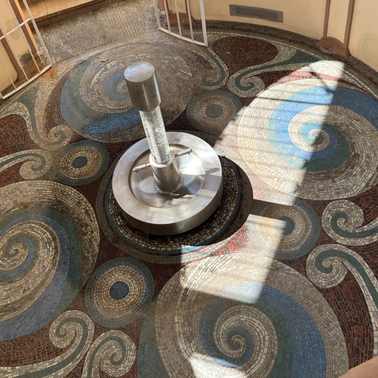 Muster mit spiralförmigen Designs und einem zentralen, metallischen Pfeiler.